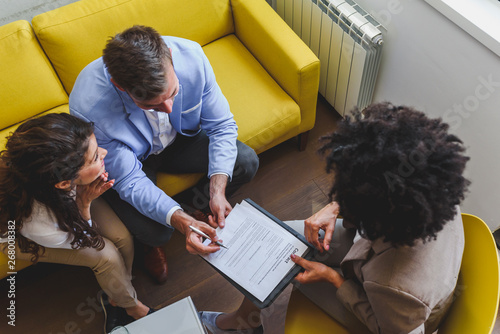 Young married couple signing real estate purchase contract  after consulting with professional broker
