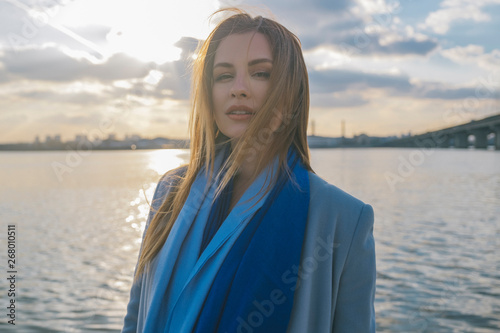 Gorgeous european woman in warm coat and dress on a walk in park near river. Windy weather. Her clothes fly in the wind. Sad, sensual and thughtful expression on her face © AnnaDemy