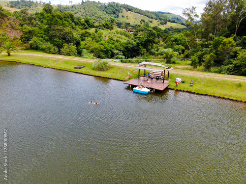Aerial view of beautiful little wood cabana next the lake in tropical mountain, with family enjoying relax sun moment, swimming and fishing. Monte Alegre Do Sul, Brazil. 