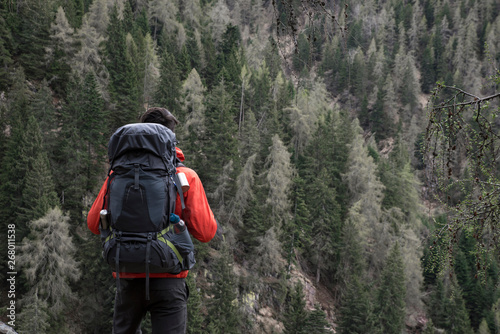Back view of a young caucasian man with a trekking backpack doing a solo adventure in the wild mountains in north Italy 