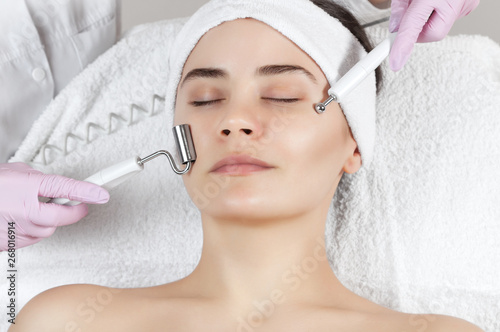 The cosmetologist makes the apparatus a procedure of Microcurrent therapy of a beautiful, young woman in a beauty salon. Cosmetology and professional skin care. photo