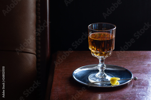 Brandy, Whiskey, Amaretto, or any Brown Liqueur Drink Served Neat with Lemon Twist in Dark Luxurious Bar photo