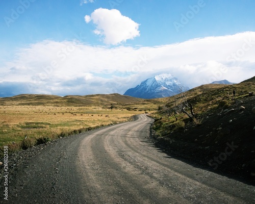 Snow capped mountains with grassy meadows in Patagonia. With Asphalt road wrapping road around hill. 