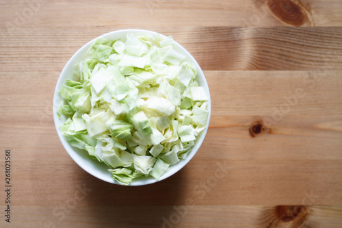 green cabbage sliced in a white plate on a wooden table and light background close-up