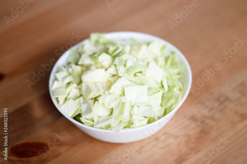 green cabbage sliced in a white plate on a wooden table and light background close-up