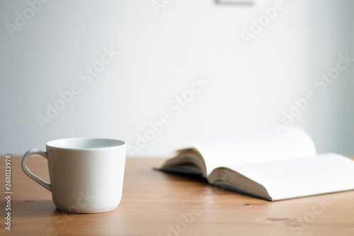 white coffee mug on wooden table and light background with book close up