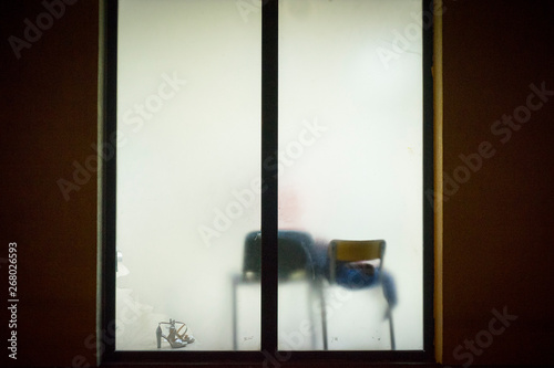 Street window with translucent glass showing two chairs and a pair of high heels women shoes in the backlit blurred light.