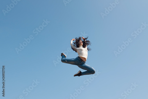 Modern young street dancer jumping high on a blue sky background. Woman flies up to the sun