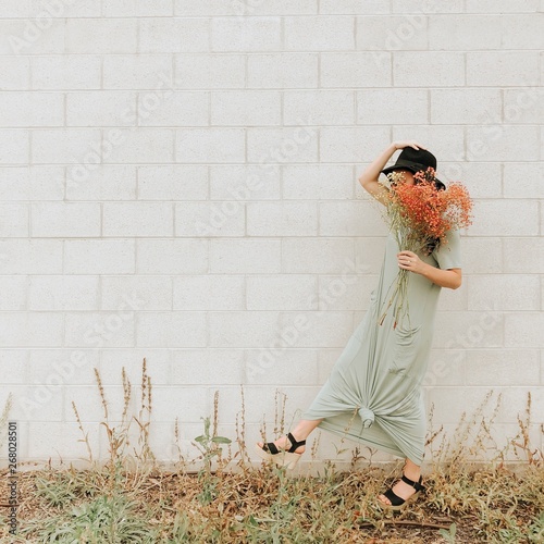 woman standing while holding orange flower near gray wall