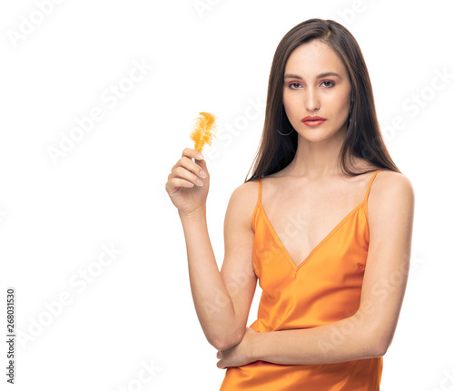 girl in orange dress on isolated background. girl in orange dress with bird feather in hand. the girl closes her right eye with a feather. the model has an orange make-up to the color of the dress