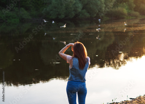 Fototapeta Naklejka Na Ścianę i Meble -  Girl photographs of birds over the river . Walking at sunset by the river