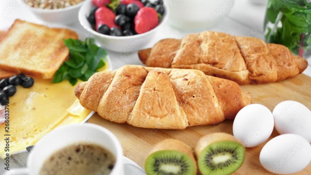 Close-up two big fresh appetizing croissant on wooden board surrounded by tasty breakfast food Close-up two big fresh appetizing croissant on wooden board surrounded by tasty breakfast food