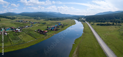 Aerial panorama of the river of Belaya with the village on its green coast, asphalt road along the river and Ural Mountains on the horizon photo