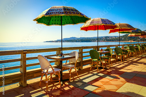 Multi-colored umbrellas against the background of the sea in coastal cafe limited by a wooden handrail.