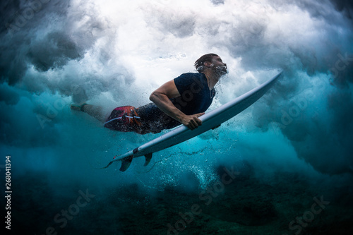 Young male surfer dives under the broken wave with his surfboard