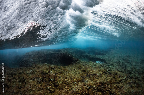 Underwater view of the ocean wave breaking over the shallow part of the coral reef at Honkeys surf spot in the Maldives