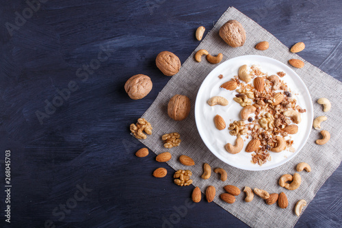 White plate with greek yogurt, granola, almond, cashew, walnuts on black wooden background.