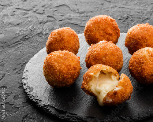 Fried potato cheese balls or croquettes with spices on black plate over dark stone background. Unhealthy food, top view. photo