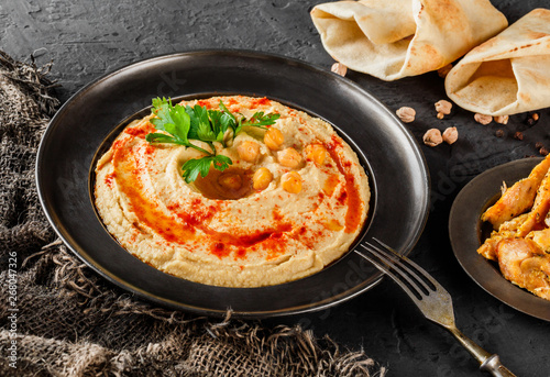 Chickpeas hummus with olive oil, paprika in a plate over dark stone background. Healthy vegan food, clean eating, dieting, top view.