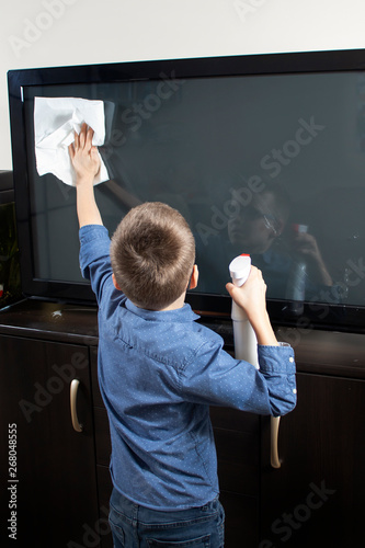 Chłopiec w okularach podczas sprzątania. Wyciera ściereczką ekran telewizora z kurzu.