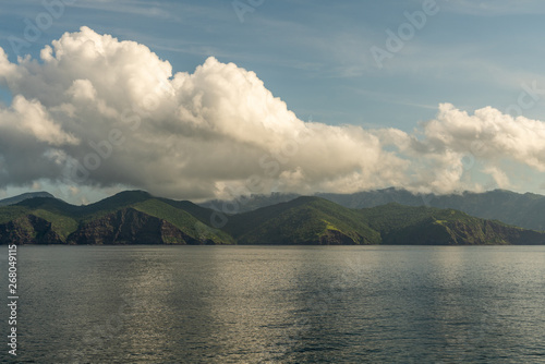 Rinca Island, Indonesia - February 24, 2019: Early morning. Southside coast in Savu Sea under cloudscape with white and darker patches.Green hills and cliffs.