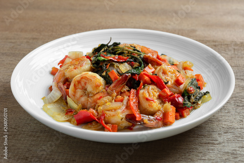 close up of stir fried shrimps with basil in a ceramic dish on wooden table. hot and spicy thai style food menu.