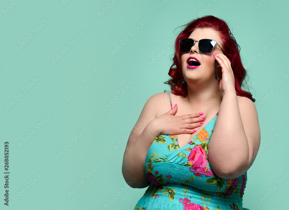 Plus-size lady overweight woman in sunglasses and colorful sundress talks on cell-phone and hear someting breathtaking Plus-size lady overweight woman in sunglasses and colorful sundress talks on cell-phone and hear someting breathtaking