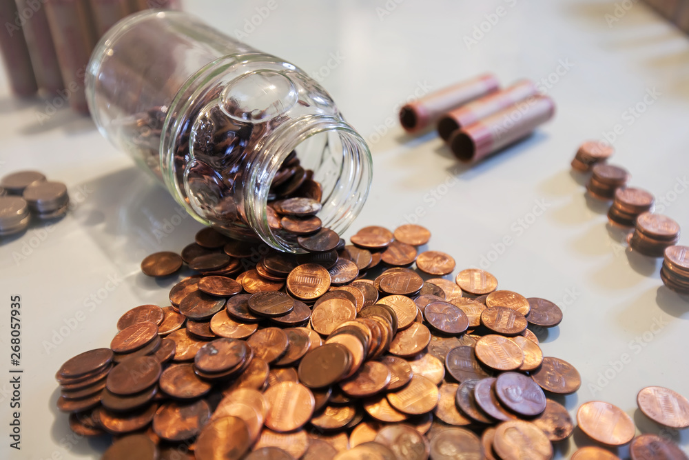 A spilled glass jar of pennies and coins from piggy bank or spare change savings. A spilled glass jar of pennies and coins from piggy bank or spare change savings.