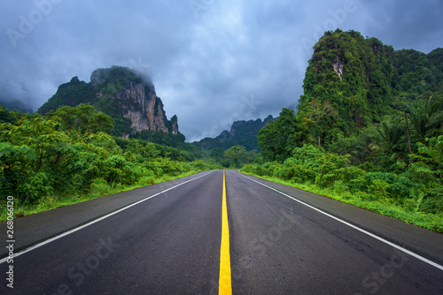 Asphalt road and mountains landscape under fog from rain with clouds