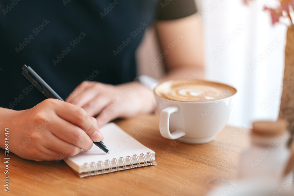 Closeup image of a woman writing on blank notebook with coffee cup on wooden table Closeup image of a woman writing on blank notebook with coffee cup on wooden table