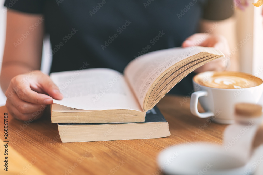 Closeup image of a woman holding and reading a vintage novel book with coffee cup on wooden table Closeup image of a woman holding and reading a vintage novel book with coffee cup on wooden table