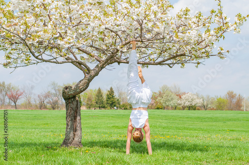 Woman is practicing yoga, doing Salamba Sirsasana exercise, standing in handstand pose near tree