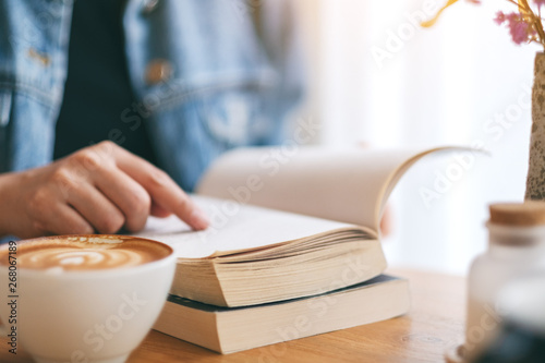 Closeup image of a woman reading and pointing at a vintage novel book with coffee cup on wooden table