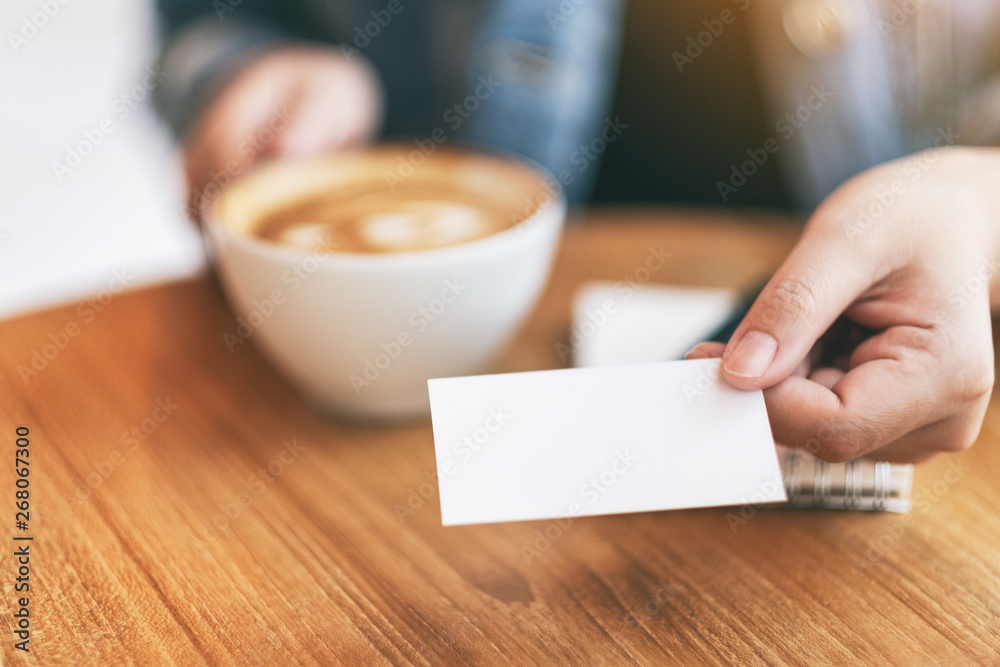 Obraz premium A woman holding and giving a blank empty business card to someone while drinking coffee