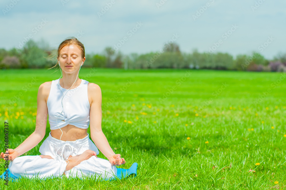 Beautiful woman is practicing yoga sitting in Lotus pose on grass Beautiful woman is practicing yoga sitting in Lotus pose on grass