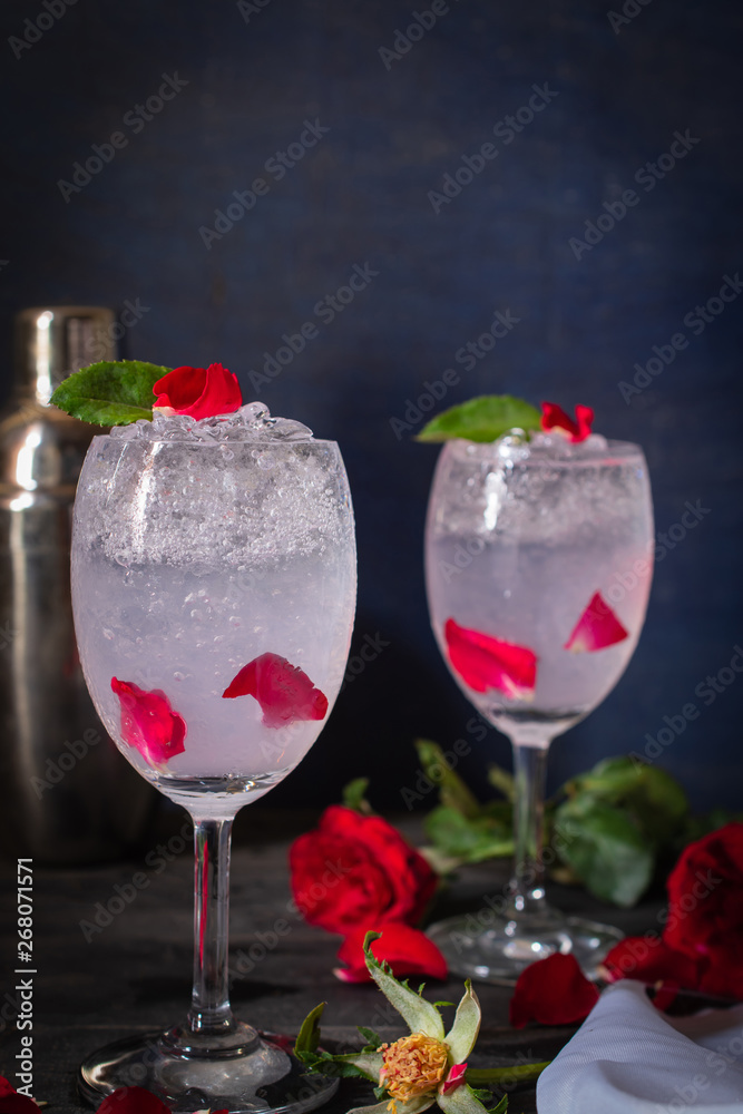 Sparkling cold water detox with rose and ice on the wood table there are rose, same object and cocktail shaker placed around. Sparkling cold water detox with rose and ice on the wood table there are rose, same object and cocktail shaker placed around.
