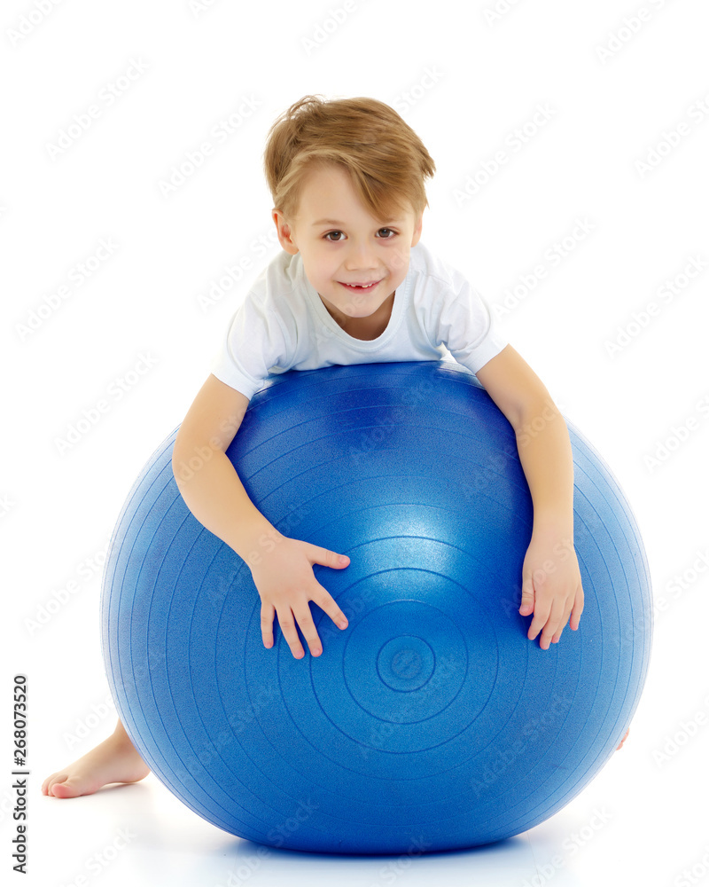 The little boy on the big ball is engaged in fitness. White T-sh The little boy on the big ball is engaged in fitness. White T-sh