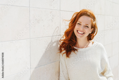 Smiling young woman near white wall photo