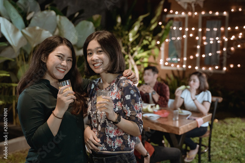two female bestfriend in garden party with friend smiling to camera