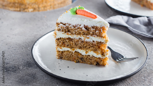 Slice of homemade carrot cake with cream cheese frosting on plate on gray stone table background