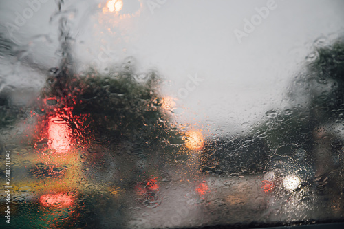 Drops Of Rain Drizzle on the glass windshield in the evening. street in the heavy rain. Bokeh Tail light and Traffic lights in city. Please drive car carefully, slippery road. soft focus.