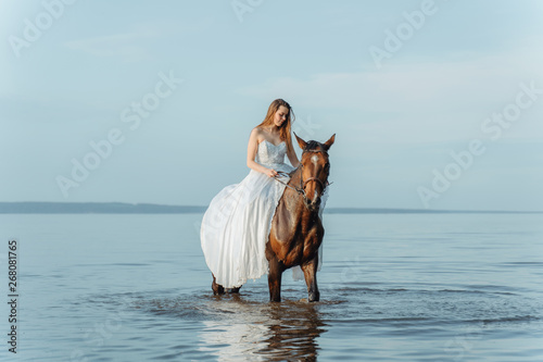 Beautiful girl in a white long dress riding a horse. Bride in the lake on horseback. © cinematri