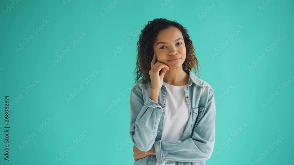 Portrait of pretty African American woman in trendy outfit thinking dreaming on blue background looking at camera and smiling. People and thoughts concept. Portrait of pretty African American woman in trendy outfit thinking dreaming on blue background looking at camera and smiling. People and thoughts concept.