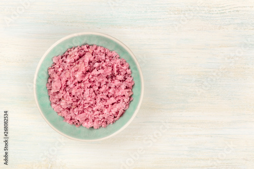 A bowl of pink Himalayan sea salt, shot from the top on a white wooden background with copy space