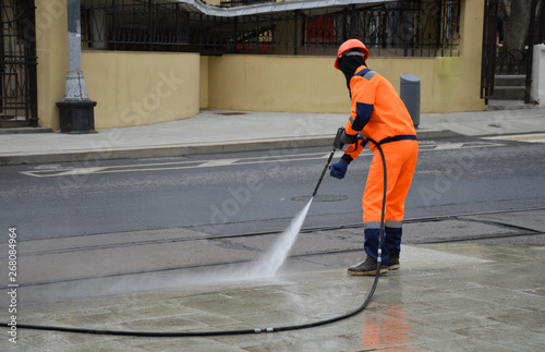 Worker washes a sidewalk from a hose