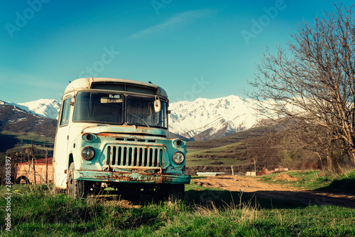Very old rusty abandoned school bus standing by the road in a small Armenian village