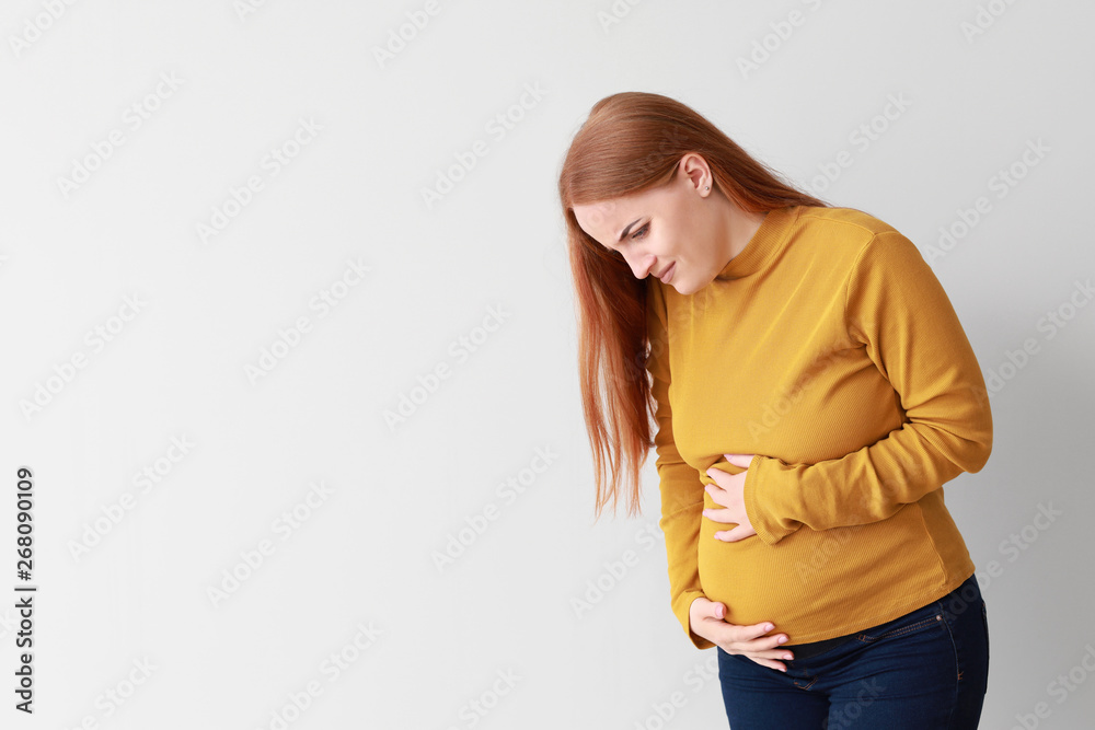 Young pregnant woman feeling bad on light background Young pregnant woman feeling bad on light background