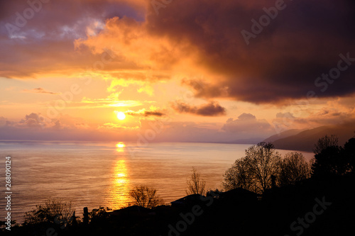 Sunset over the sea. Big orange clouds over mountains and water. Coastline. Storm off shore. Evening light.