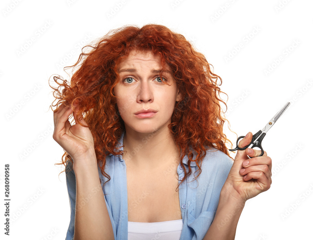 Obraz premium Beautiful woman displeased with her hair holding scissors on color background
