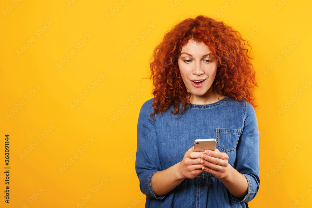 Surprised redhead woman with mobile phone on color background - obrazy, fototapety, plakaty 